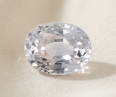 Natural oval-cut light peach sapphire gemstone on ivory fabric