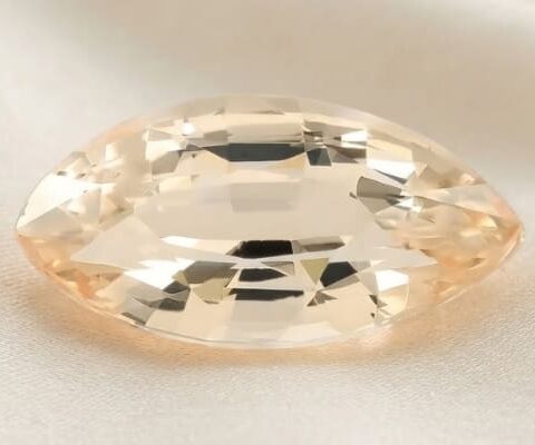 Natural marquise-cut golden peach sapphire gemstone on ivory fabric