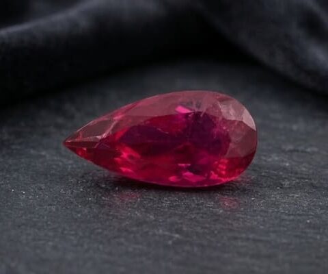 Natural Rubellite Tourmaline gemstone with rich raspberry-red color and pear cut, angled view.