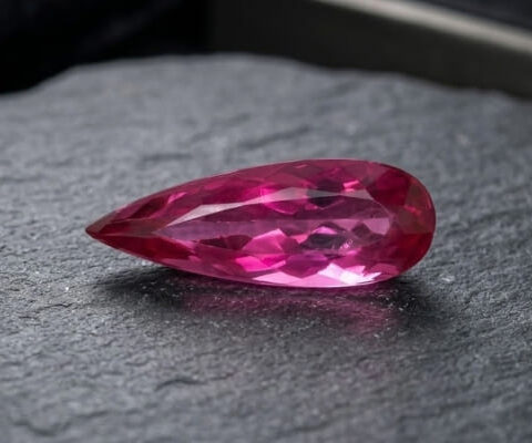 Natural Rubellite Tourmaline gemstone with vibrant raspberry-pink color and pear cut, angled view.