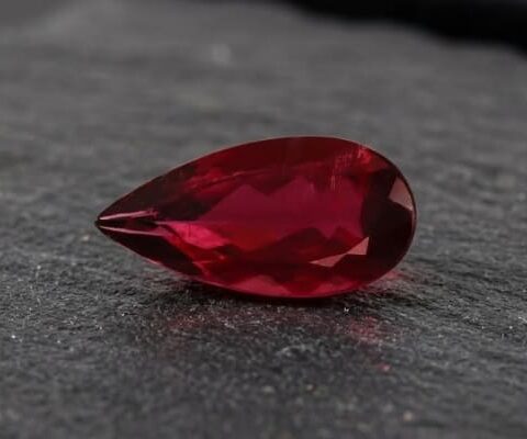 Natural Rubellite Tourmaline gemstone with deep ruby-red color and pear cut, angled view.