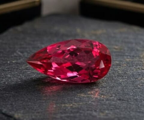 Natural Rubellite Tourmaline gemstone with vibrant raspberry-red color and pear cut, angled view.