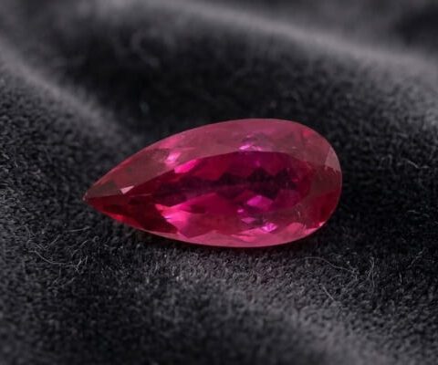 Natural Rubellite Tourmaline gemstone with vibrant raspberry-pink color and pear cut, angled view.