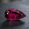 Natural Rubellite Tourmaline gemstone with deep raspberry-pink color and pear cut, angled view.