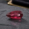 Natural Rubellite Tourmaline gemstone with rich raspberry-red color and pear cut, angled view.