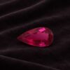 Natural Rubellite Tourmaline gemstone with vibrant raspberry-red color and pear cut, angled view.
