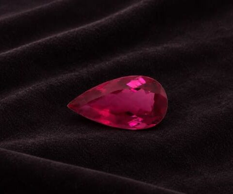 Natural Rubellite Tourmaline gemstone with vibrant raspberry-red color and pear cut, angled view.