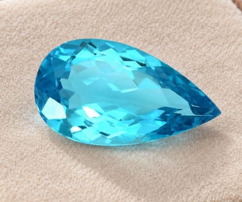 Pear-cut sea blue Apatite gemstone with brilliant facets on a beige jewellery display.