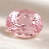 Natural soft pink oval-cut morganite gemstone on cream fabric.