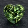 Natural unheated heart-cut blue green sapphire gemstone on dark stone surface.