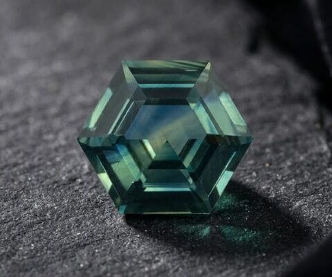 Natural unheated hexagonal-cut green blue sapphire gemstone on dark fabric.