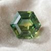 Natural unheated hexagonal-cut green yellow blue sapphire gemstone on soft cream fabric.