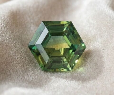 Natural unheated hexagonal-cut green yellow blue sapphire gemstone on soft cream fabric.