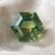 Natural unheated hexagonal-cut green yellow blue sapphire gemstone on soft cream fabric.