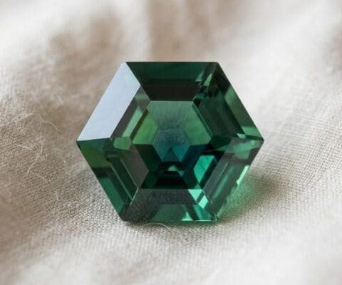 Natural unheated hexagonal-cut greenish blue sapphire gemstone on soft cream fabric.