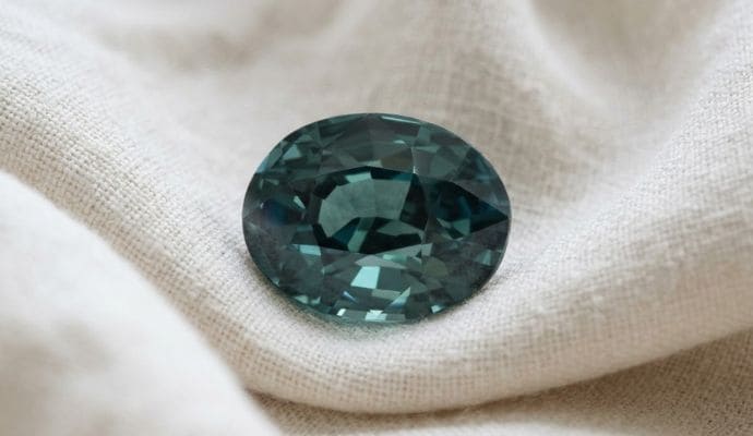 Natural unheated oval-cut greenish blue sapphire gemstone on soft cream fabric.