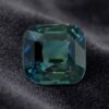 Natural unheated cushion-cut greenish blue sapphire gemstone on dark velvet fabric.