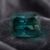 Natural unheated emerald-cut greenish blue sapphire gemstone on dark velvet fabric.