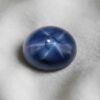 Natural oval blue star sapphire gemstone with visible star effect on soft cream fabric.