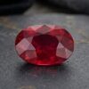 Natural unheated oval-cut Mozambique ruby gemstone on dark stone surface.